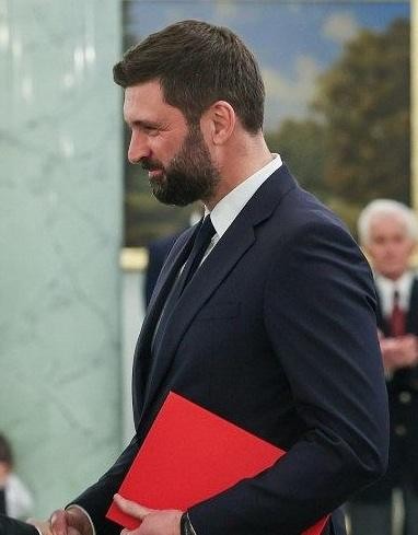 Nikodem Rachoń w tle sugerującym działalność dyplomatyczną lub politykę międzynarodową, z wyrazem skupienia i profesjonalizmu.