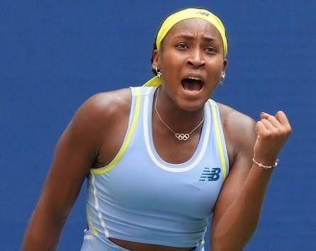 Coco Gauff celebrująca zwycięstwo na korcie tenisowym, z uniesionymi rękami w geście triumfu i wiwatującym tłumem w tle.
