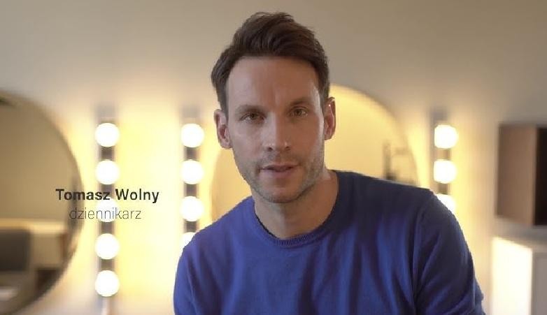 Tomasz Wolny, prezenter telewizyjny, w dynamicznym ujęciu w studiu telewizyjnym, podczas prowadzenia programu.