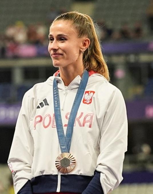 Natalia Bukowiecka biegnąca na torze w Olsztynie, z jeziorem w tle, symbolizującym jej miejsce zamieszkania i treningów.