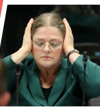 Scena z sali sądowej lub posiedzenia parlamentarnego, ukazująca intensywną debatę prawną lub polityczną.