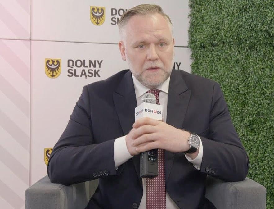 Dawid Jackiewicz podczas wystąpienia publicznego, z gestykulacją, na tle rozmytej publiczności, symbolizujący jego zaangażowanie w życie publiczne i kampanię prezydencką.