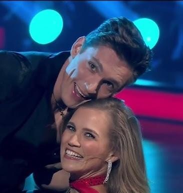 Agnieszka Kaczorowska w eleganckim stroju tanecznym, wykonująca dynamiczną figurę w studiu, prezentująca swoje mistrzostwo w tańcu.