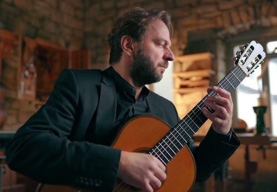 Marcin Dylla podczas dynamicznego występu na scenie, grający na gitarze klasycznej, z widocznymi dłońmi i ekspresyjną twarzą.