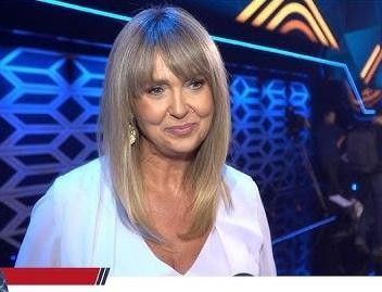 Ewa Wachowicz w kuchni, ubrana w elegancki strój kucharza, aktywnie gotująca lub prezentująca danie, z uśmiechem na twarzy, w tle nowoczesna kuchnia.