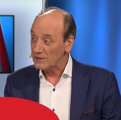 Dariusz Szpakowski w kabinie komentatorskiej, z ekspresyjną mimiką i mikrofonem, oddający pasję i emocje towarzyszące jego relacjom sportowym.