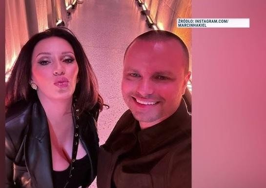 Marcin Hakiel uśmiechnięty, trzymający smartfon, symbolizujący jego aktywność na Instagramie i kontakt z fanami.