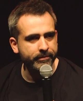 Abelard Giza podczas występu stand-upowego na scenie, w otoczeniu rozmytej publiczności i dynamicznego oświetlenia.