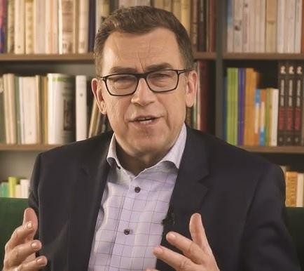 Maciej Orłoś z książką dla dzieci, w swobodnej pozie, symbolizującej jego rolę jako autora i ojca.