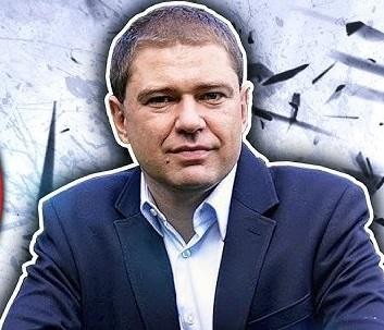 Piotr Szumlewicz aktywnie przemawiający na publicznym wydarzeniu, z mikrofonem w ręku, w tle zamazanej publiczności lub sceny, co symbolizuje jego rolę jako lidera i publicysty.