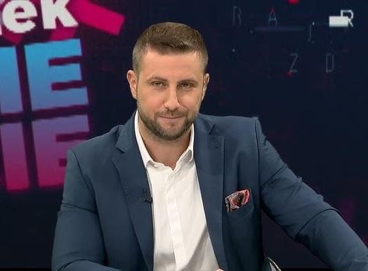 Miłosz Kłeczek w studiu telewizyjnym, z mikrofonem, wyrażający intensywne emocje podczas ożywionej dyskusji, z rozmytym tłem studia.