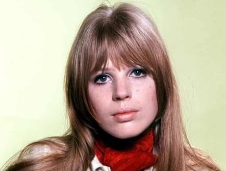 Marianne Faithfull na scenie w latach 70., uchwycona w dynamicznym ujęciu podczas występu, z mikrofonem w dłoni i intensywnym wyrazem twarzy.
