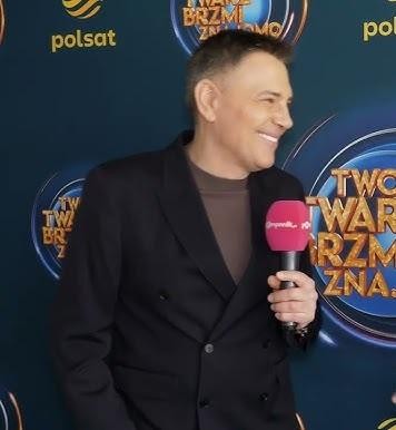 Zbliżenie na uśmiechniętą twarz Krzysztofa Ibisza, prezentującego swoją charyzmę, z subtelnie rozmytym tłem.